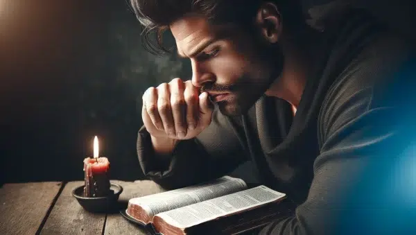 Imagen de un hombre reflexionando con una Biblia abierta y una vela encendida